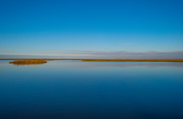 Shore of a blue lake in wetland under a bright blue sky, Almere, Flevoland, The Netherlands, January 1, 2021