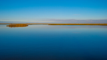 Shore of a blue lake in wetland under a bright blue sky, Almere, Flevoland, The Netherlands, January 1, 2021