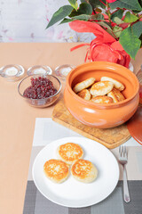 sweet cottage cheese pancakes in a plate and a clay pot, with jam on a server table Delicious cottage cheese dessert