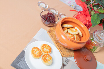 sweet cottage cheese pancakes in a plate and a clay pot, with jam on a server table Delicious cottage cheese dessert