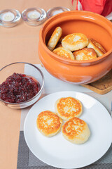 sweet cottage cheese pancakes in a plate and a clay pot, with jam on a server table Delicious cottage cheese dessert