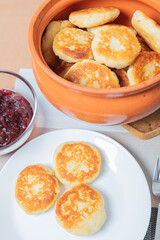 sweet cottage cheese pancakes in a plate and a clay pot, with jam on a server table Delicious cottage cheese dessert