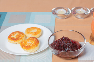sweet cottage cheese pancakes in a plate and a clay pot, with jam on a server table Delicious cottage cheese dessert