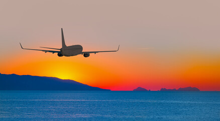 Airplane flying over tropical sea at beautiful light sunset or dramatic sky 