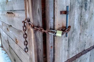 Closed wood door of outdoor bathrooom with rusty chain and long shackle padlock