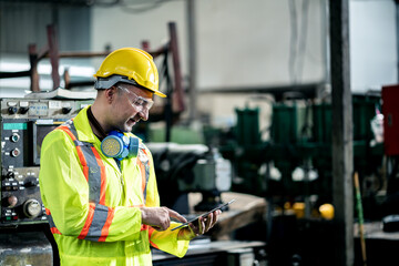 engineer / worker man caucasian in protective safety jumpsuit uniform with yellow hardhat and using digital tablet at factory.Metalworking industry concept professional engineer manufacturing machine