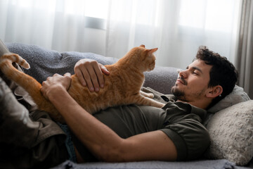 young man lying on the sofa and brown tabby cat , look at each other