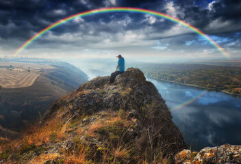 rainbow over the river. man on a cliff above the canyon