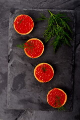 Tartlets with red salmon caviar on black stone plate, decorated with green dill, close - up. Copy space. Seafood appetizer