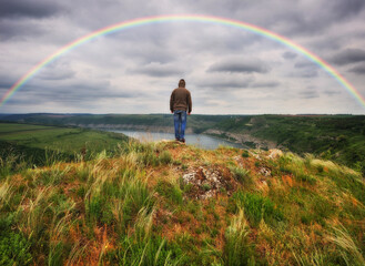 rainbow over the river. man on a cliff above the canyon