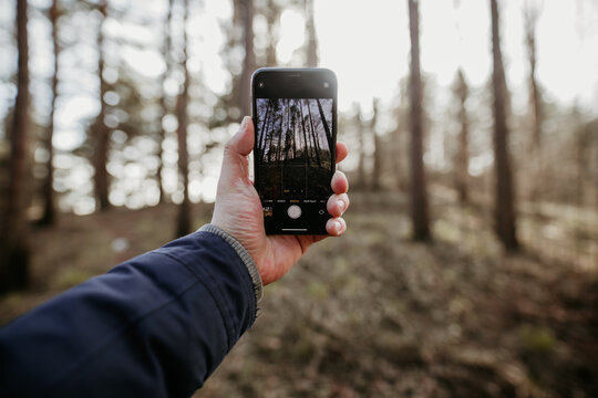 mans arm taking picture with mobile device in a forest
