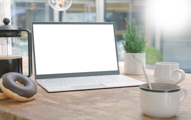 Generic laptop computer and coffee cup resting on wooden table. Blank screen for mockup