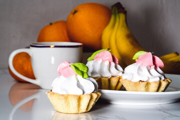 Meringue cakes in a basket next to a cup of hot tea and fruits