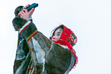 A young girl, in the national winter clothes of the northern inhabitants of the tundra, takes a...