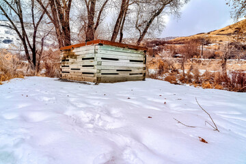 Wooden storage shed with rusty metal roof on snow covered landscape in winter
