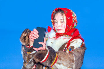 A young girl, in the national winter clothes of the northern inhabitants of the tundra, takes a selfie on a smartphone