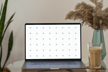 Laptop's front view mock-up with coffee and flower home decor in vase on glass table, with plant in background, blank screen for your design, with free space for your text about business