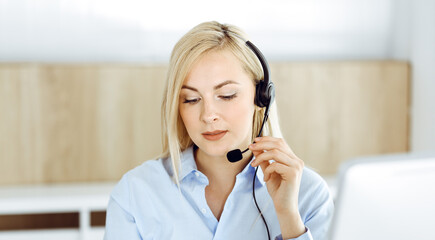 Blonde business woman sitting and communicated by headset in call center office. Concept of telesales business or home office occupation