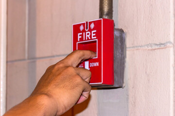 Hand pulling down the manual fire alarm station in case of fire emergency