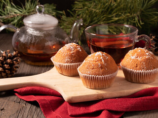 Muffins on wooden board with cup of tea. Cupcakes on background of pine branches. Festive background.