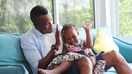 African American father playing with his little daughter who is learning from digital tablet from home on sofa couch - Powered by Adobe