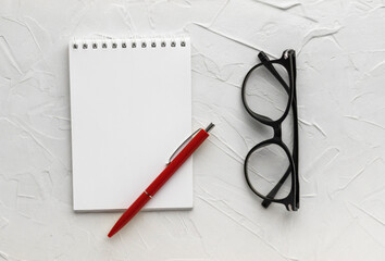 Blank notepad, pen and eyeglasses on white putty texture background. Business concept. Notebook for...