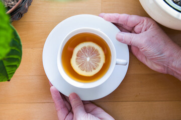 Human hands holding a white cup of tea with lemon. Flat lay view