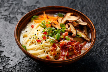 Pork bone Japanese style ramen noodle soup with crispy bacon, shiitake mushrooms and spring onions in clay bowl