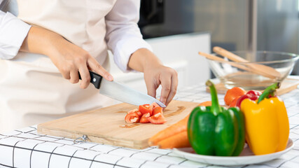 Obraz na płótnie Canvas young Asian woman is preparing healthy food vegetable salad by Cutting tomato for ingredients on cutting board on light kitchen, Cooking At Home and healthy food concept.