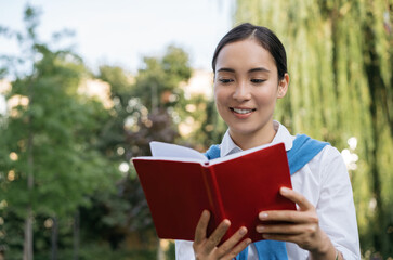 Close up portrait of beautiful asian woman reading book. Smiling student studying, learning language, sitting in park, education concept 
