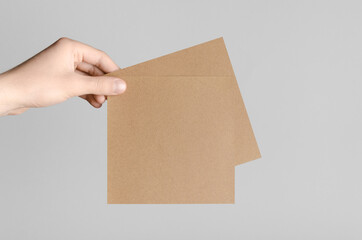 Kraft Square Flyer / Invitation Mock-Up - Male hands holding kraft flyers on a gray background.