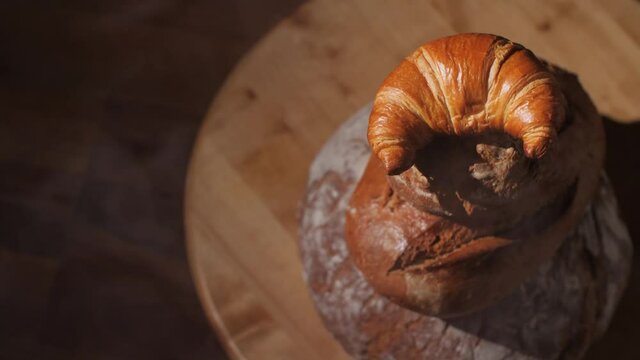 A freshly baked croissant and organic bread loaves on wood background. Tower of traditional French pastry and rustic German wholewheat bread. Delicious brown background with copy space. 4K.