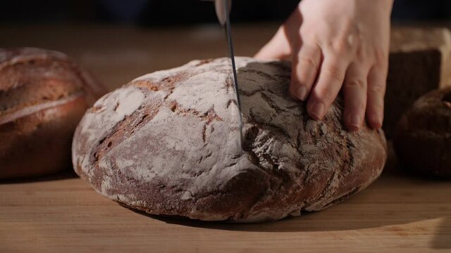 Cutting of a fresh, homemade and organic bread loaf with flour on rustic crust. Slicing of baked whole-grain bread in a traditional artisan bakery, Tasty and healthy food. 4K.