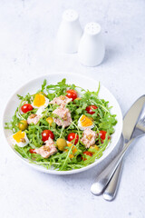 Salad with tuna, arugula, tomatoes, olives and eggs in a white plate. A traditional dish. Close-up.