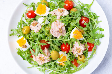 Salad with tuna, arugula, tomatoes, olives and eggs in a white plate. A traditional dish. Close-up.