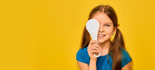 Positive girl having an eye exam with one eye covering using a special tool, on a yellow background. Eye test for child