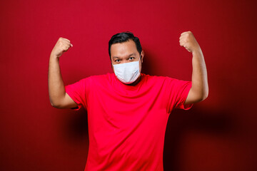 Young asian man wearing a medical face mask while raise his hand up to encourage and protects against the spread of corona virus disease