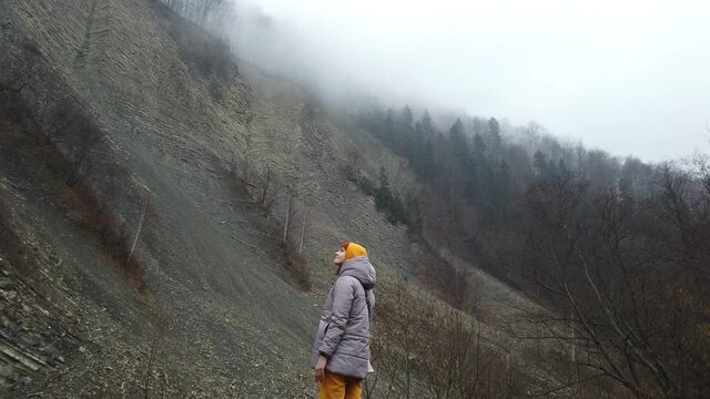 Young woman traveler in yellow pants and hoodie enjoying picturesque view of mountain cliff. Traveling at the nature. spreads his arms to the sides and brings them over his head