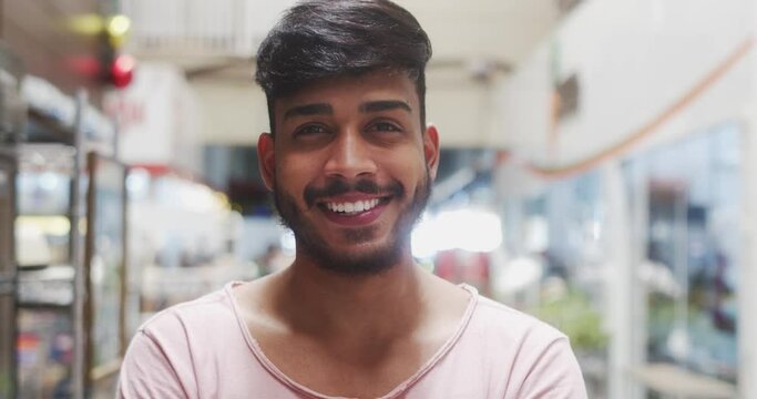 Young Brazilian man smiling in a marketplace. Latin man smiling to camera. 4K.