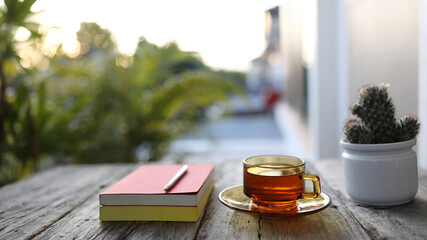tea in clear transparent glass and notebooks with pencil on wooden table at outdoor