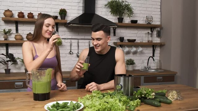 Making Green Juice At Home: Young Sporty Couple In Sportswear Drinking Smoothie From A Glass. Healthy Breakfast After A Workout In The Kitchen 4k