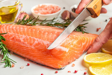 Cooking fresh raw salmon fish fillet with spices, herbs and lemon. Man cutting a piece from salmon fillet