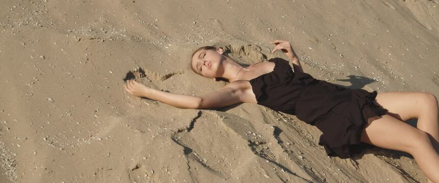 Charming cute slim young woman in black short dress lying elegantly on white sand