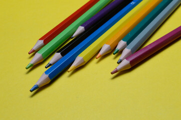 several multi-colored pencils lie on the yellow surface.