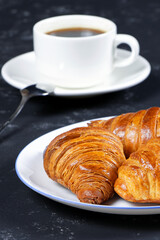 A cup of hot coffee and croissants on a black background. Breakfast with coffee and fresh pastry. Coffee beans on a table. Fresh cake and pastry. Vertical orientation.