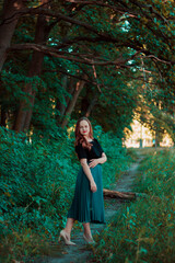 Girl in a turquoise skirt in a fairy forest. Smiling cute girl with red lipstick. Girl on the background of large tree branches