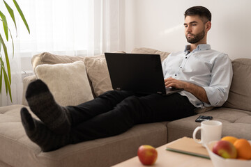 Man lying on sofa at home and working on laptop