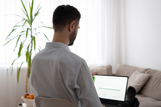 Man Sitting At Home On A Chair And Working On A Laptop, Light Background, View From The Back