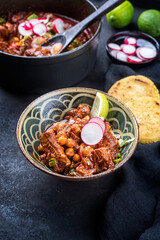 Modern style traditional slow cooked Mexican pozole rojo with tortilla served as close-up in a design bowl on a rustic board