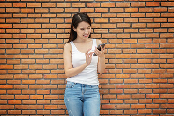 Smiling young woman using a smartphone againts brick wall